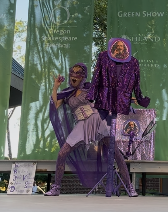 Jenifer Joy posing in a purple cape beside the Shakespeare costume stand during the show finale