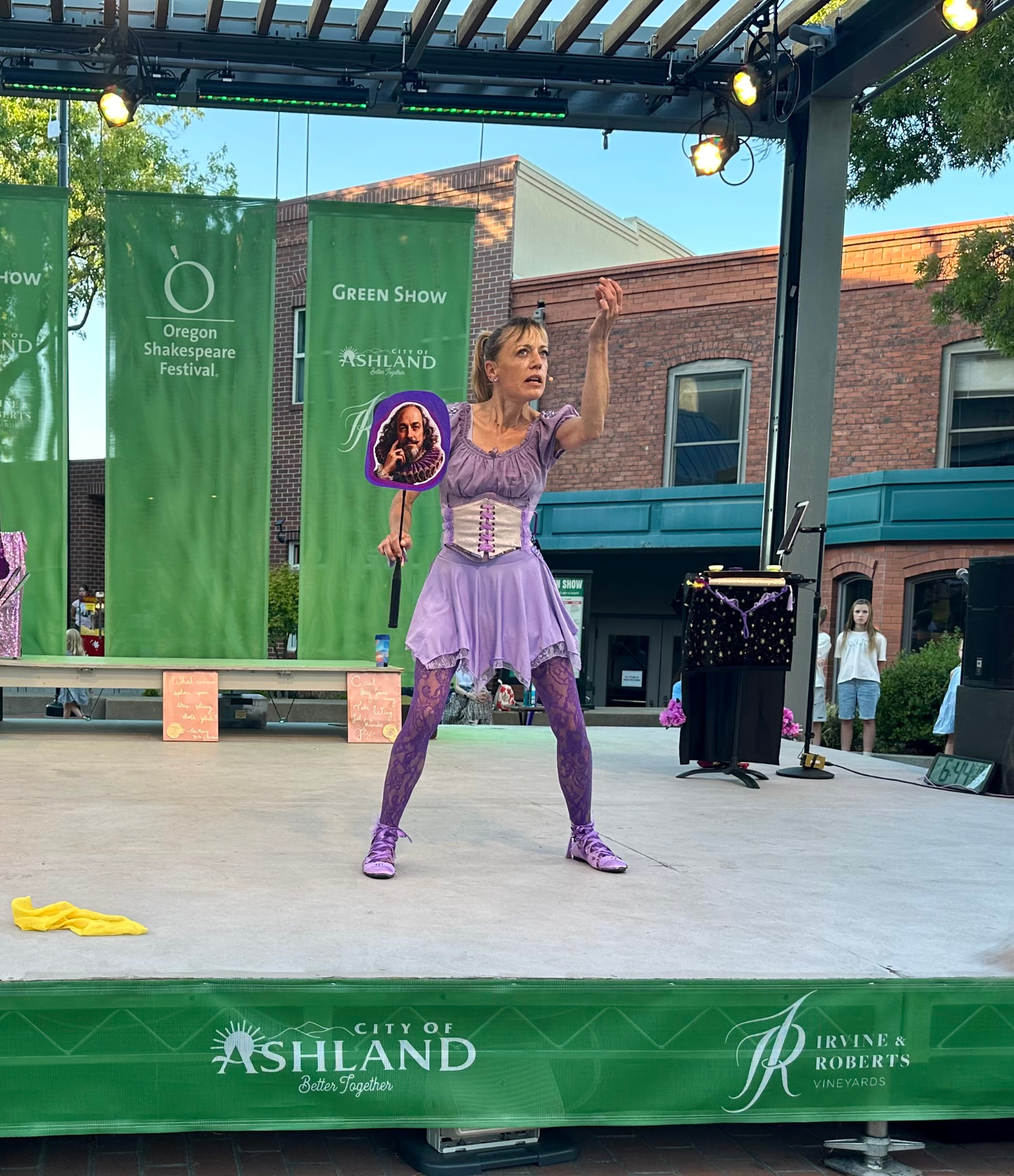 Jenifer Joy holding a Shakespeare fan and gesturing to the audience on the Green Show stage in Ashland